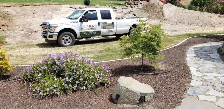 Flagstone path through curbed mulch beds with a Japanese maple and a boulder, an OMG truck behind