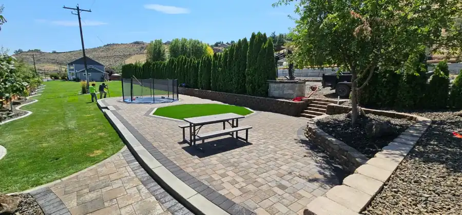 Backyard with paver terraces, block steps, a retaining wall and a curbed lawn