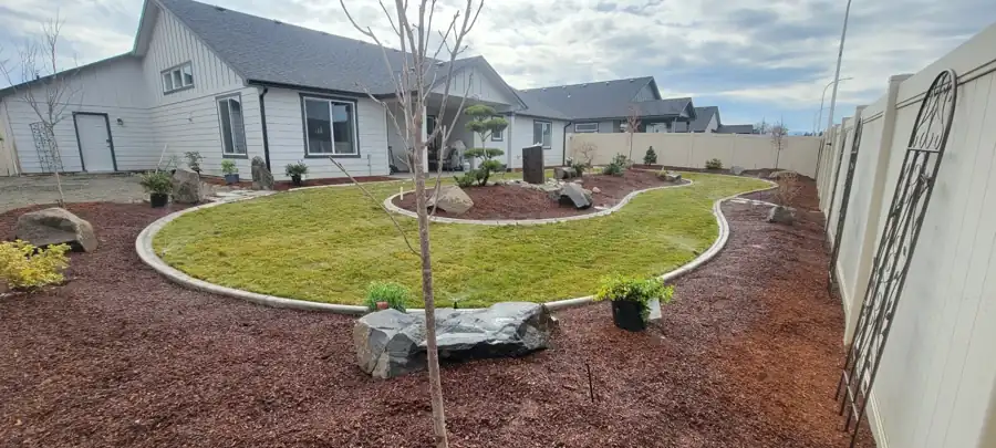 New lawn inside a curbed kidney bed with red mulch and young trees